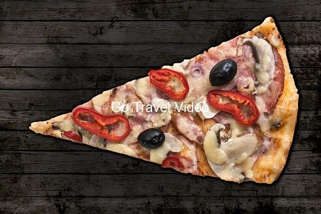 A pizza with tomatoes olives and cheese on a wooden surface Description automatically generated with low confidence