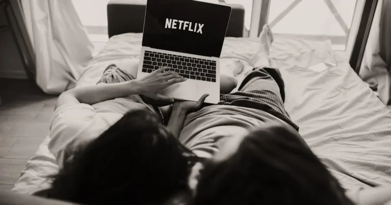 A couple relaxing together, watching Netflix on a laptop in a cozy bedroom setting.