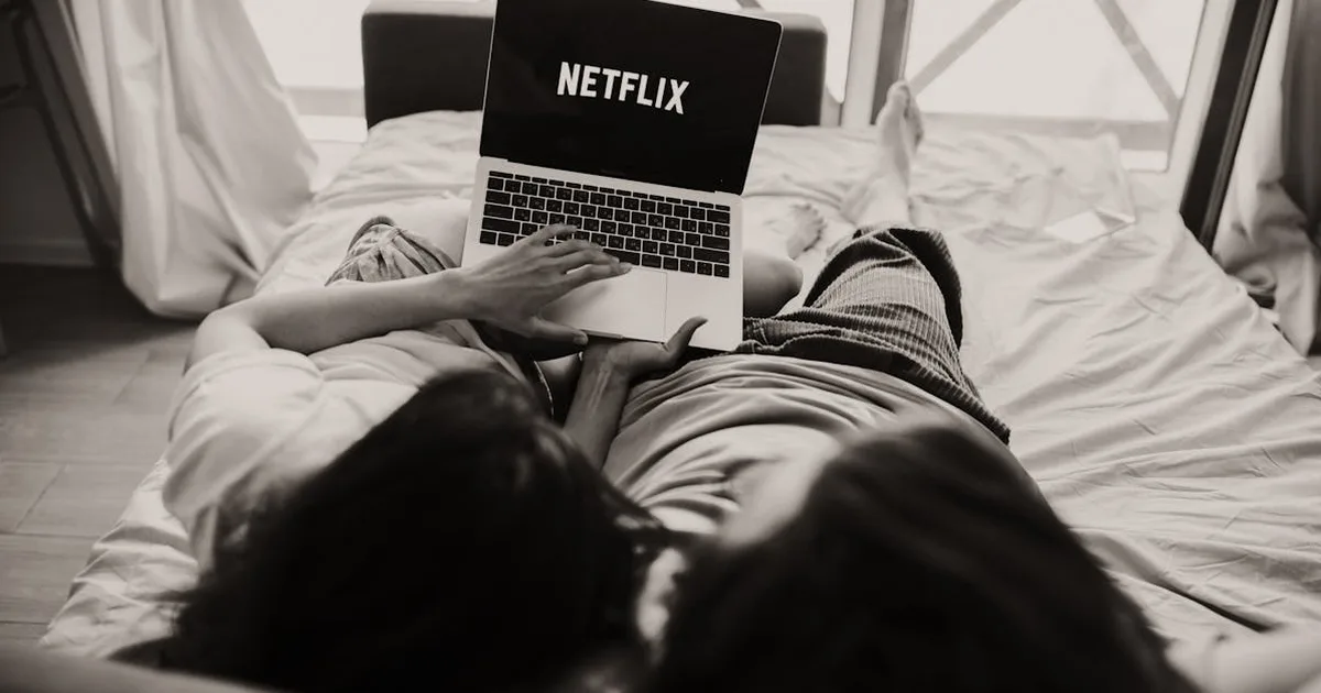 A couple relaxing together, watching Netflix on a laptop in a cozy bedroom setting.