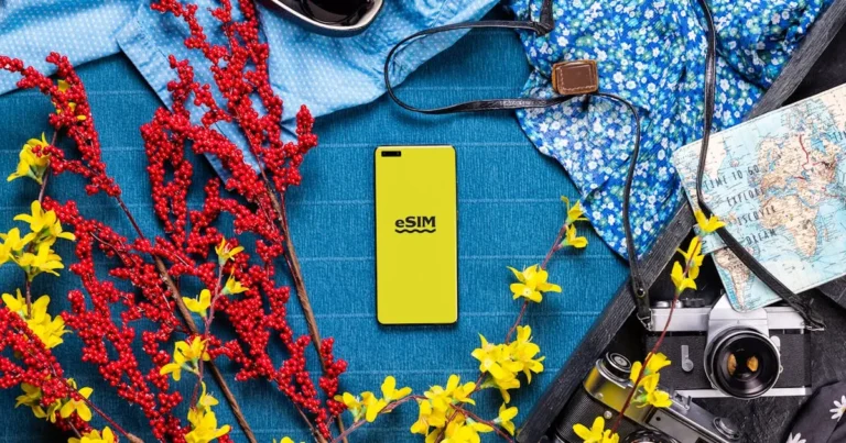 Flat lay of travel essentials including smartphone, camera, and vibrant flowers on a colorful backgr